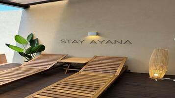 A modern outdoor seating area with wooden loungers and a wall-mounted sign that reads "STAY AYANA".