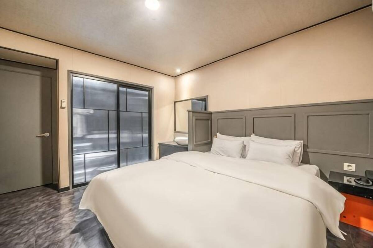 Habitación de hotel con una cama grande, una mesita de noche, un espejo y una puerta que da a un balcón.