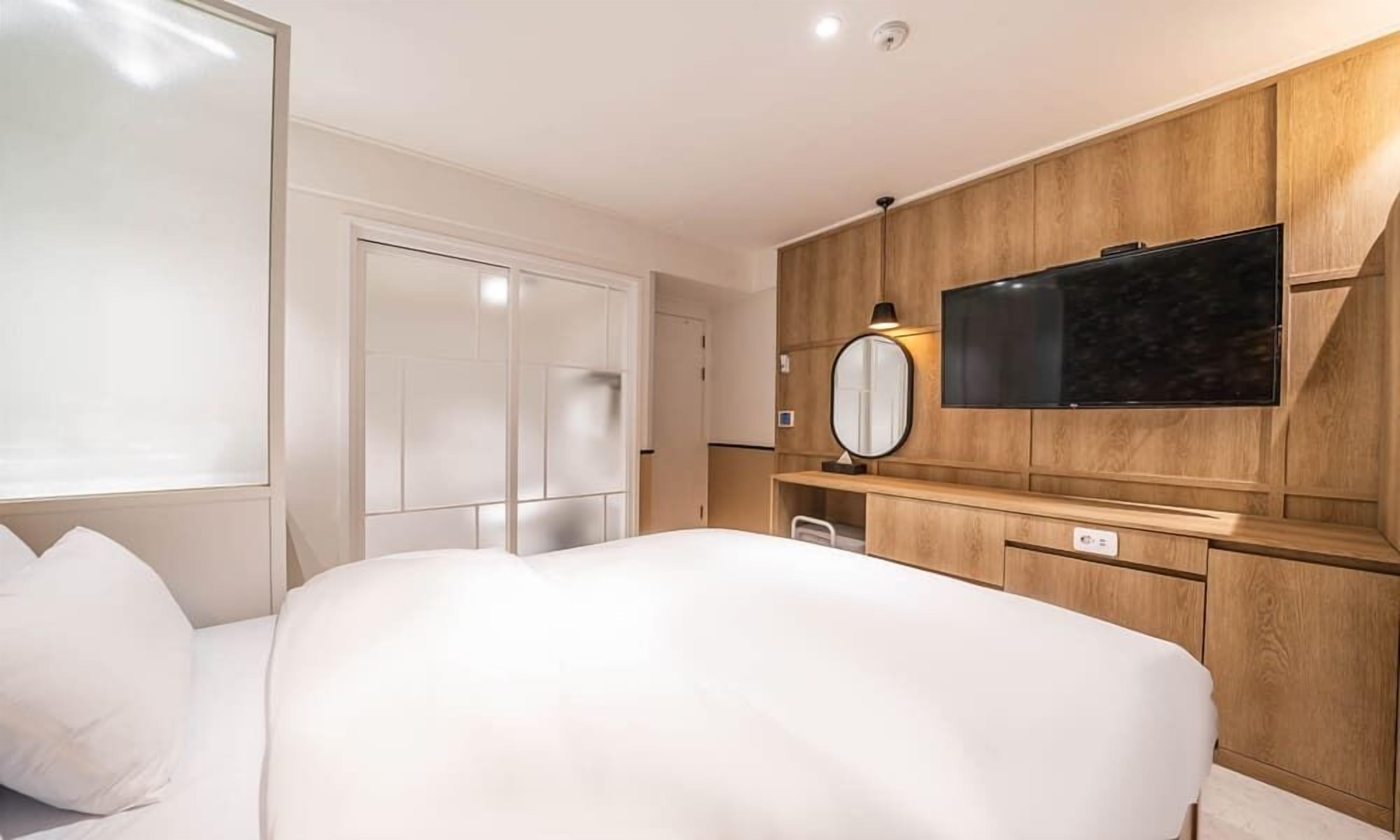 Ein Hotelzimmer mit einem großen Bett, einem an der Wand montierten Fernseher, einem Spiegel und einem Kleiderschrank.