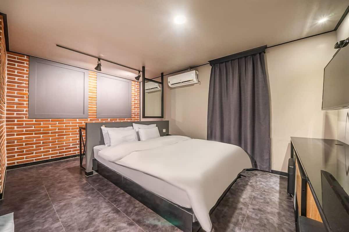 Una habitación de hotel moderna con pared de ladrillo decorativa, una cama grande, un televisor de pantalla plana y un espejo sobre la cama.