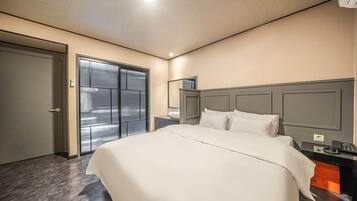 A modern hotel room with a large bed, a bedside table, a nightstand, a mirror, and a wardrobe.