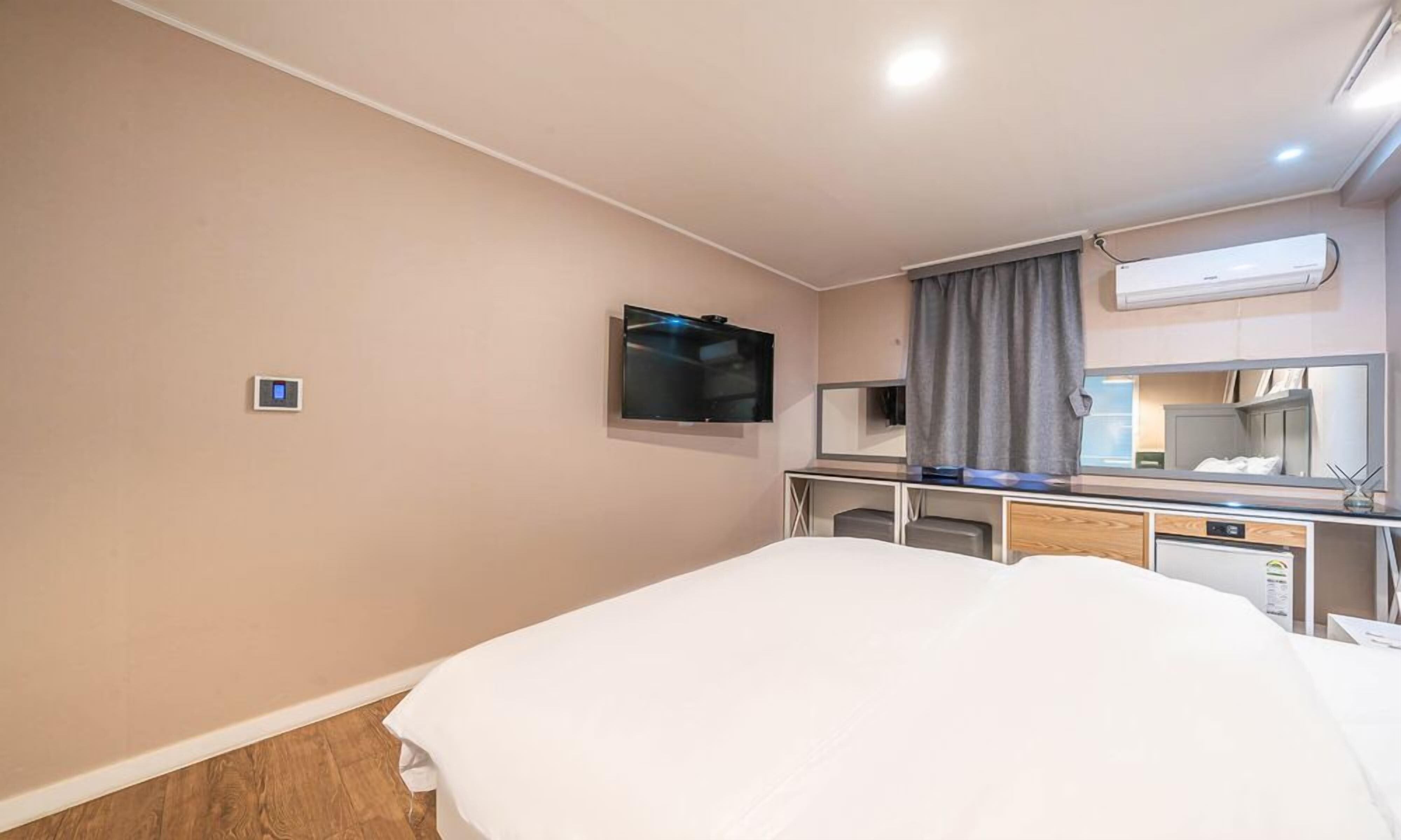 Habitación de hotel con cama, televisión montada en la pared, escritorio con espejo y aire acondicionado.