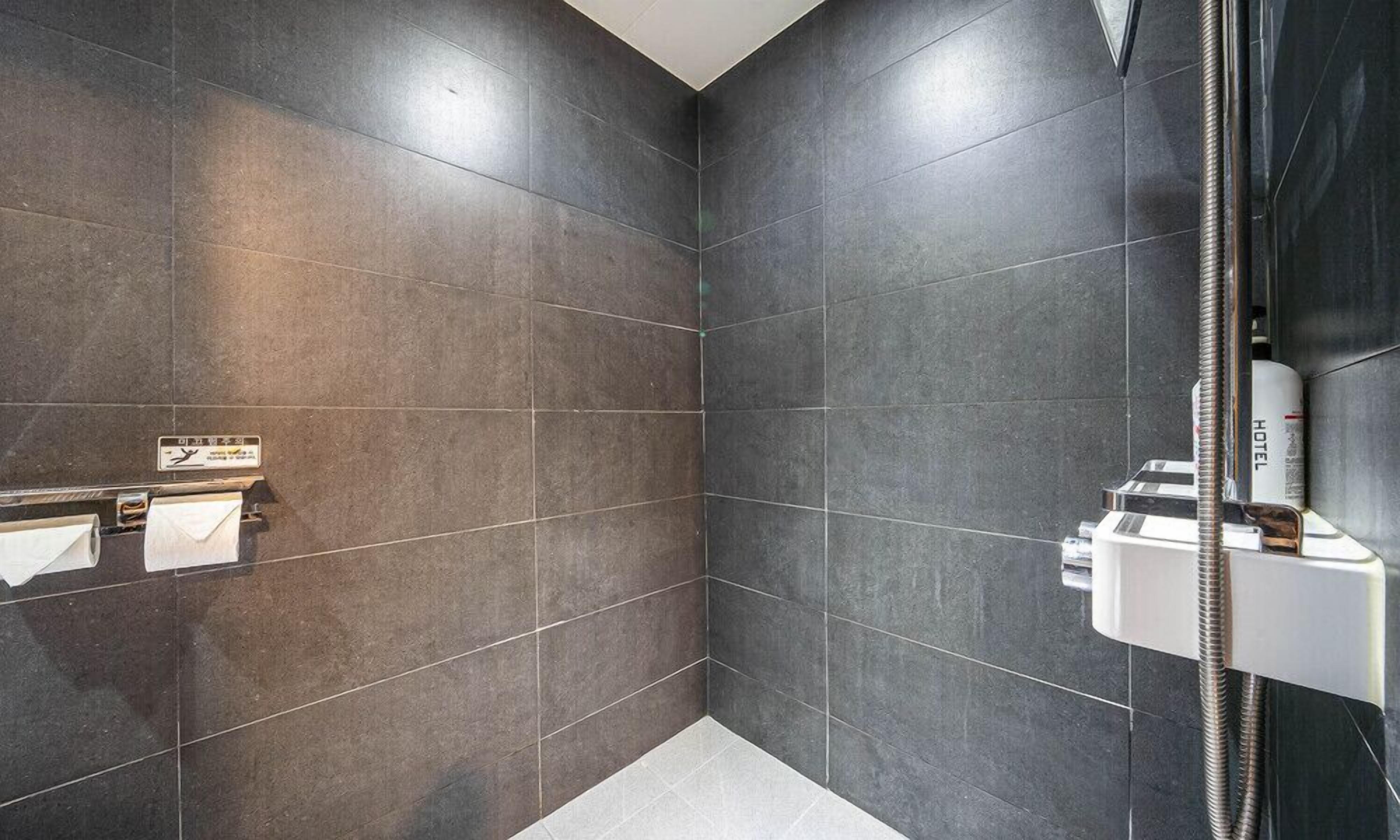A modern bathroom with dark tiles, a shower, and a towel rack with a sign.