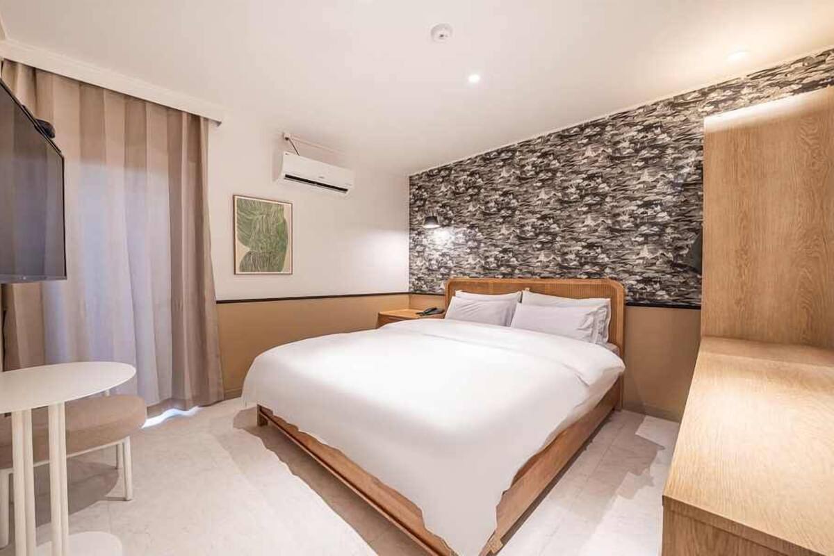 Una habitación de hotel moderna con una cama grande, una mesita, un televisor y un detalle decorativo en la pared.