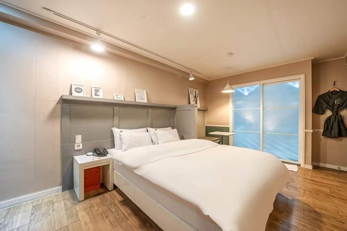 Un dormitorio con una cama grande, mesitas de noche, una mesita auxiliar, una ventana con vistas y una puerta.