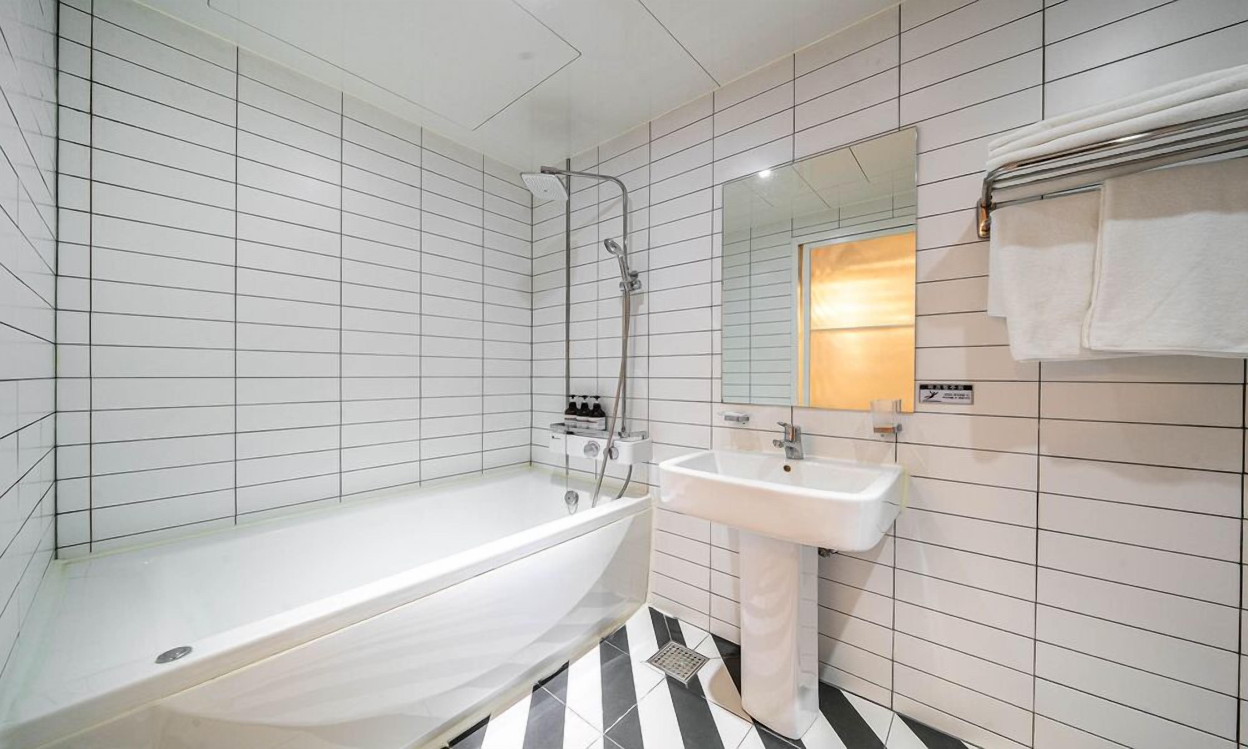 Un baño moderno con bañera, lavamanos y ducha. Las paredes están cubiertas de azulejos, y hay un espejo sobre el lavamanos.