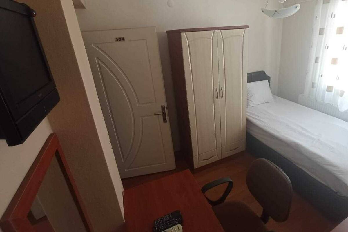 Quarto pequeno com uma cama, escrivaninha, cadeira, guarda-roupa e porta.