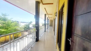 A corridor with a balcony, a view of greenery, and a building with yellow walls. - Sasando Residence Kupang (Kupang)
