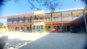 A multi-story building with a red roof, balconies, and a paved courtyard. - Sasando Residence Kupang (Kupang)