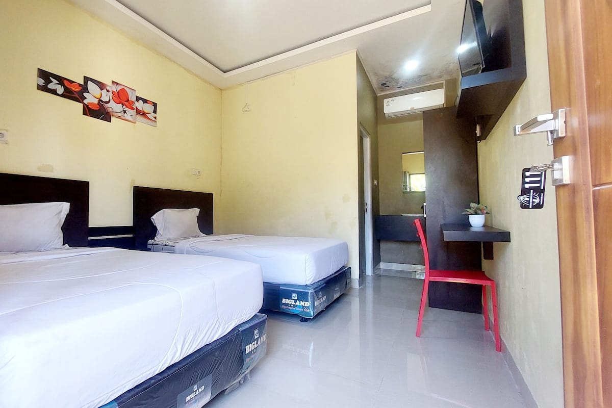 A hotel room with two beds, a small desk, a chair, a television, and a door with a number sign.