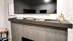 Una sala moderna con chimenea, un televisor de pantalla plana grande montado encima y una mesita con una lámpara y un cactus.