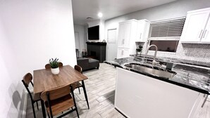 Una cocina moderna con comedor, que incluye una mesa de madera, sillas, una isla integrada con pileta y muebles de cocina blancos.
