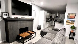 Una sala de estar moderna con un sofá gris, una mesa de centro de madera y un televisor de pantalla plana sobre una chimenea.