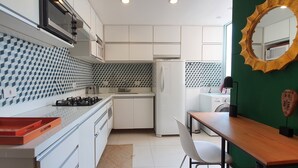 A compact kitchen with white cabinets, a patterned backsplash, a stove, and a microwave. - Moderno e Vibrante na Augusta (São Paulo)