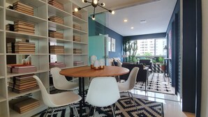 A modern room with a round wooden table, white chairs, and a bookshelf filled with books. - Moderno e Vibrante na Augusta (São Paulo)