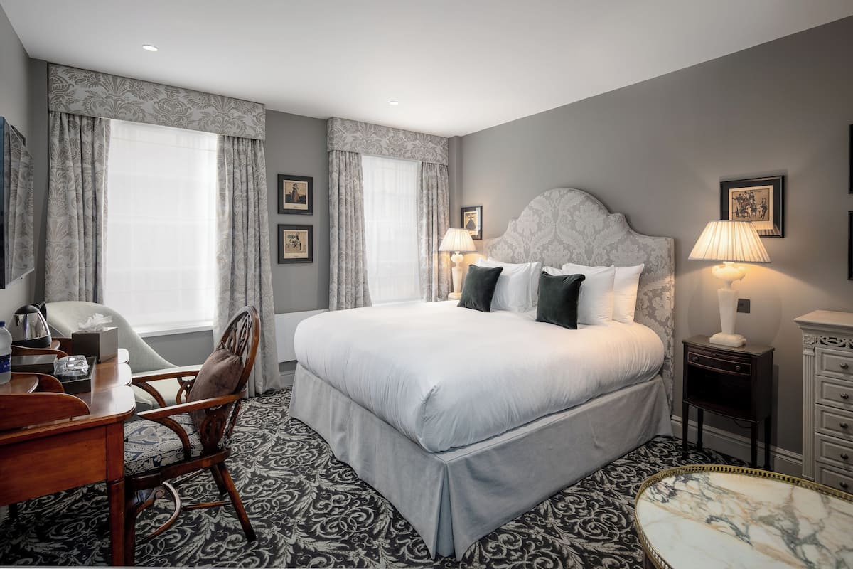 A hotel room with a large bed, two bedside lamps, a desk with a chair, and a patterned carpet.