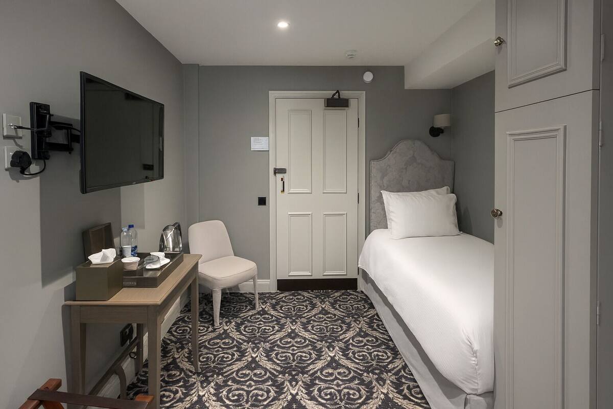 A hotel room with a bed, a desk with a chair, a television, and a patterned floor.