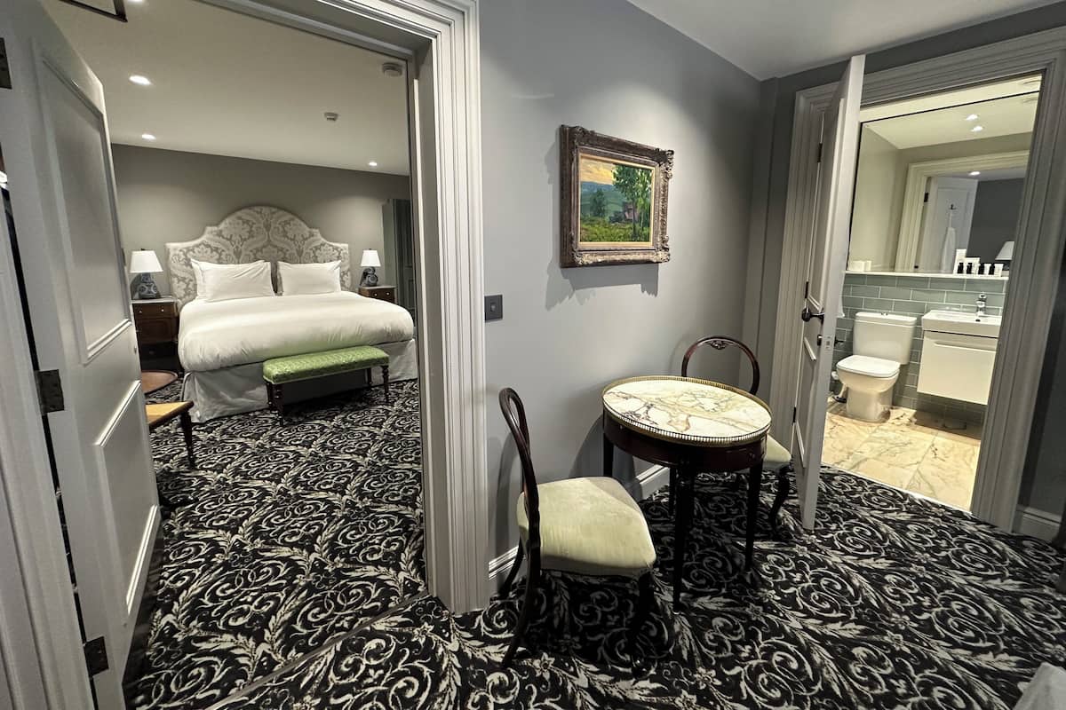 A hotel room with a bed, bedside table, lamp, chair, and a view of the bathroom.