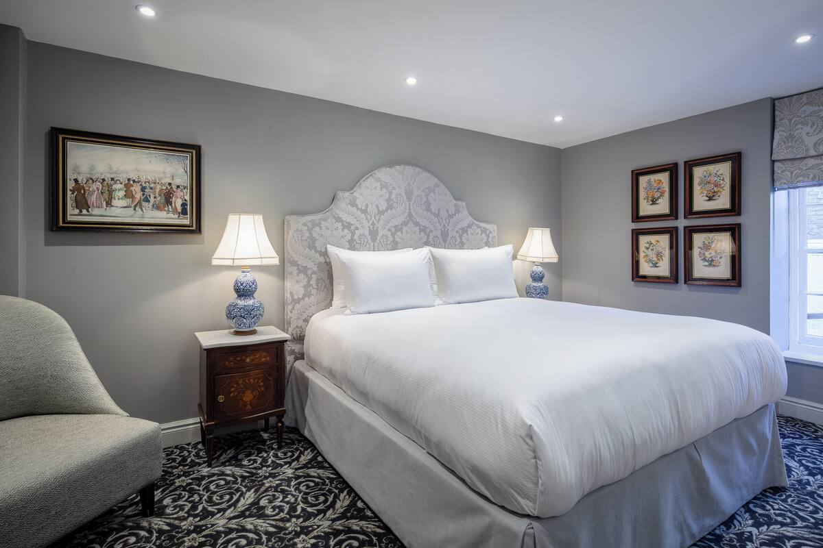 A neatly arranged bedroom with a large bed, two bedside tables with lamps, a chair, and a patterned carpet.