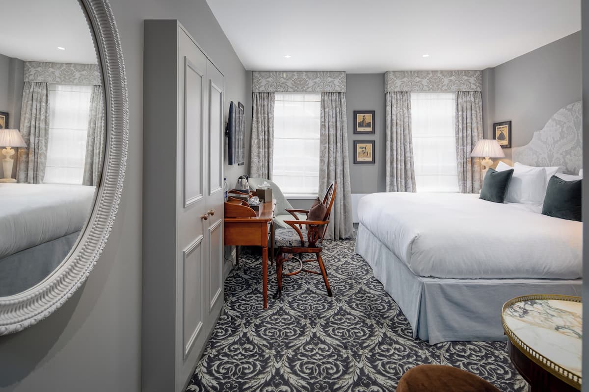 A hotel room with two beds, a desk, a chair, a round table, and a large mirror.