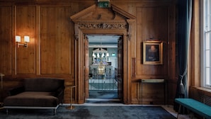 A wooden-paneled hallway with a staircase leading to a dining area, a framed portrait, and a bench. - No. 30 Knightsbridge (London)