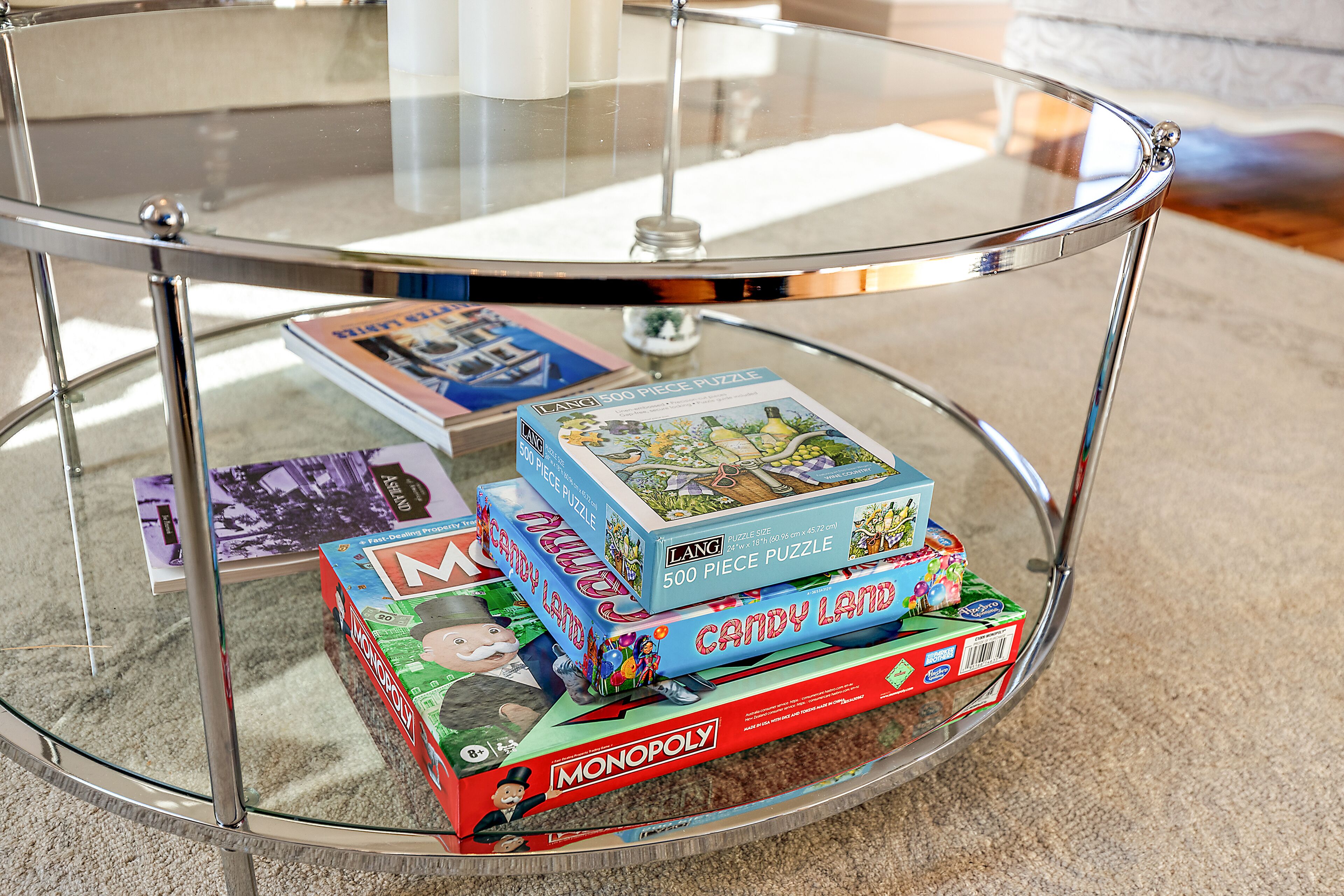 A glass-top table with several board games, including Candy Land and Monopoly, on a carpeted floor.