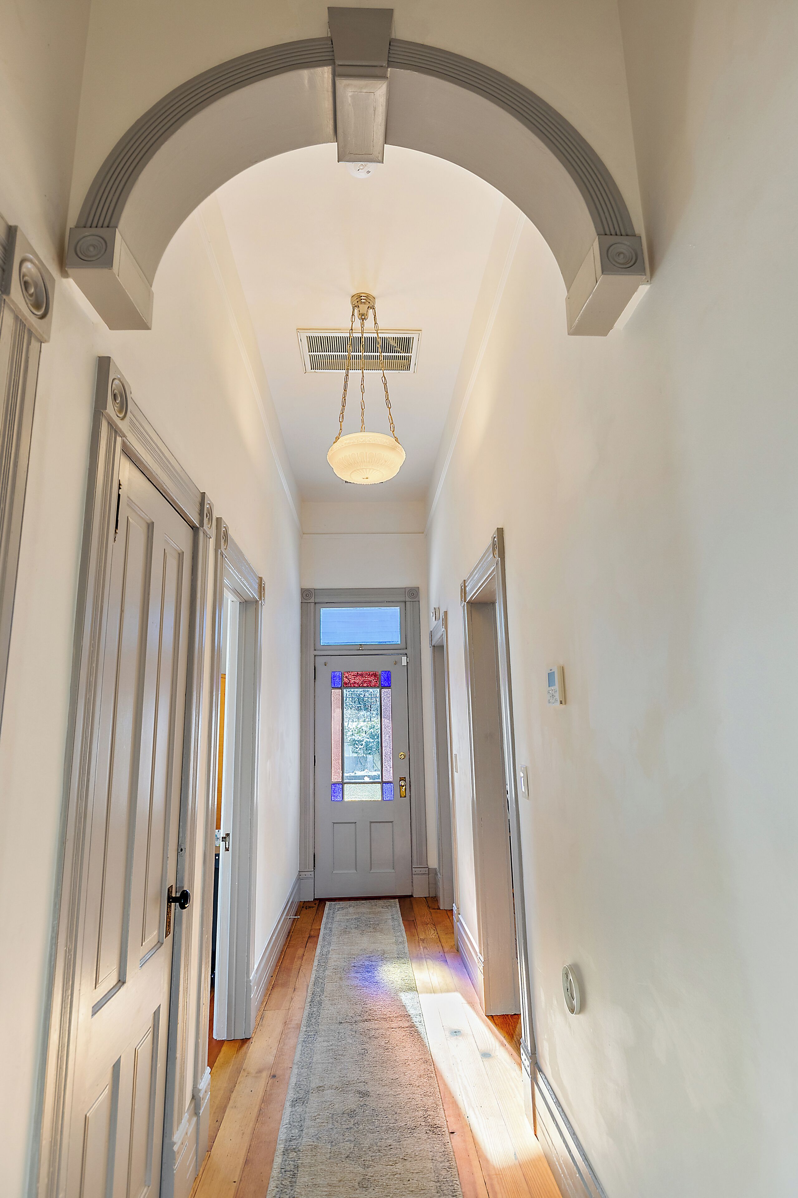 A hallway with white walls, wooden floors, and a ceiling fan.