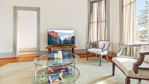 A living room with a glass coffee table, a television, a chair, and a view of mountains through the window. - Barclay Klum House by WanderLodges (Ashland)