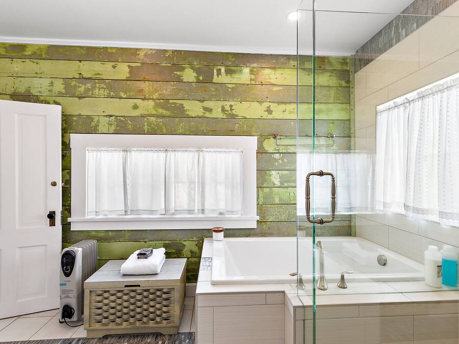 Een badkamer met een groene houten wand, een witte badkuip, een glazen douchecabine en een witte deur.