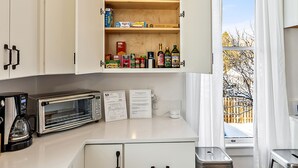 A kitchen with white cabinets, a microwave, and a window with curtains. - Barclay Klum House by WanderLodges (Ashland)