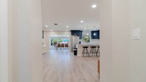 Una cocina moderna con una isla central, armarios blancos y un comedor con sillas.