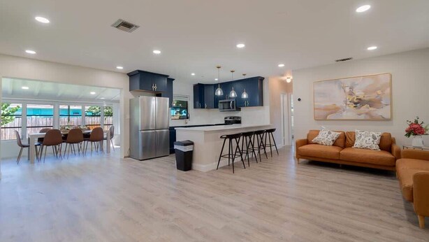 Una cocina moderna con una isla central, taburetes de bar y un comedor con sillas.
