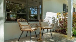 Un espacio al aire libre con sillas de mimbre, una pequeña mesa redonda, ventanas amplias y vistas del entorno.
