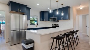 Una cocina moderna con armarios azul marino, electrodomésticos de acero inoxidable y una isla central con taburetes de bar.
