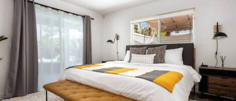 A modern bedroom with a large bed, a bench, a desk, and a window with a view.