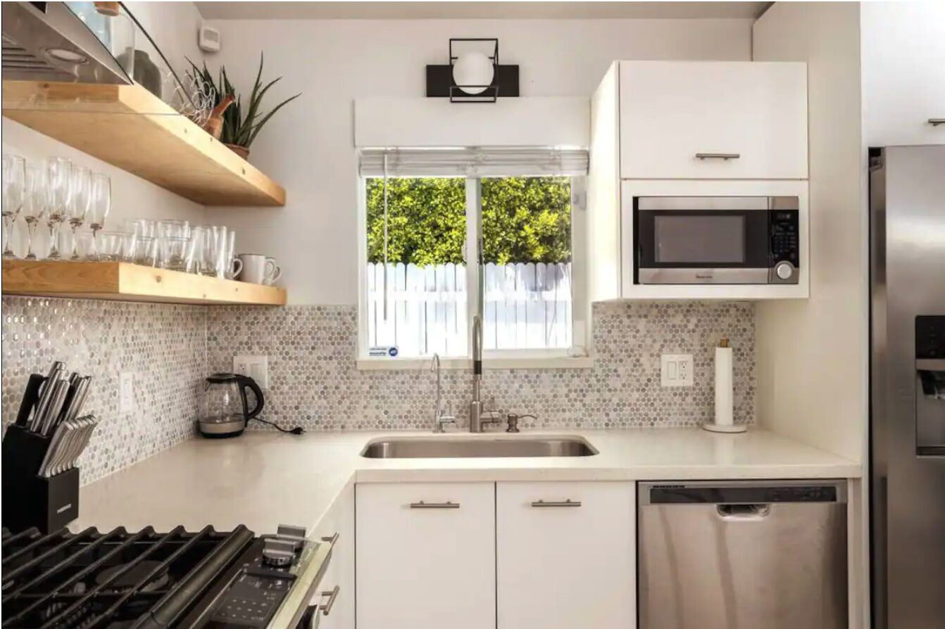 A modern kitchen with white cabinets, a stainless steel dishwasher, a microwave, and a window with a view of greenery.
