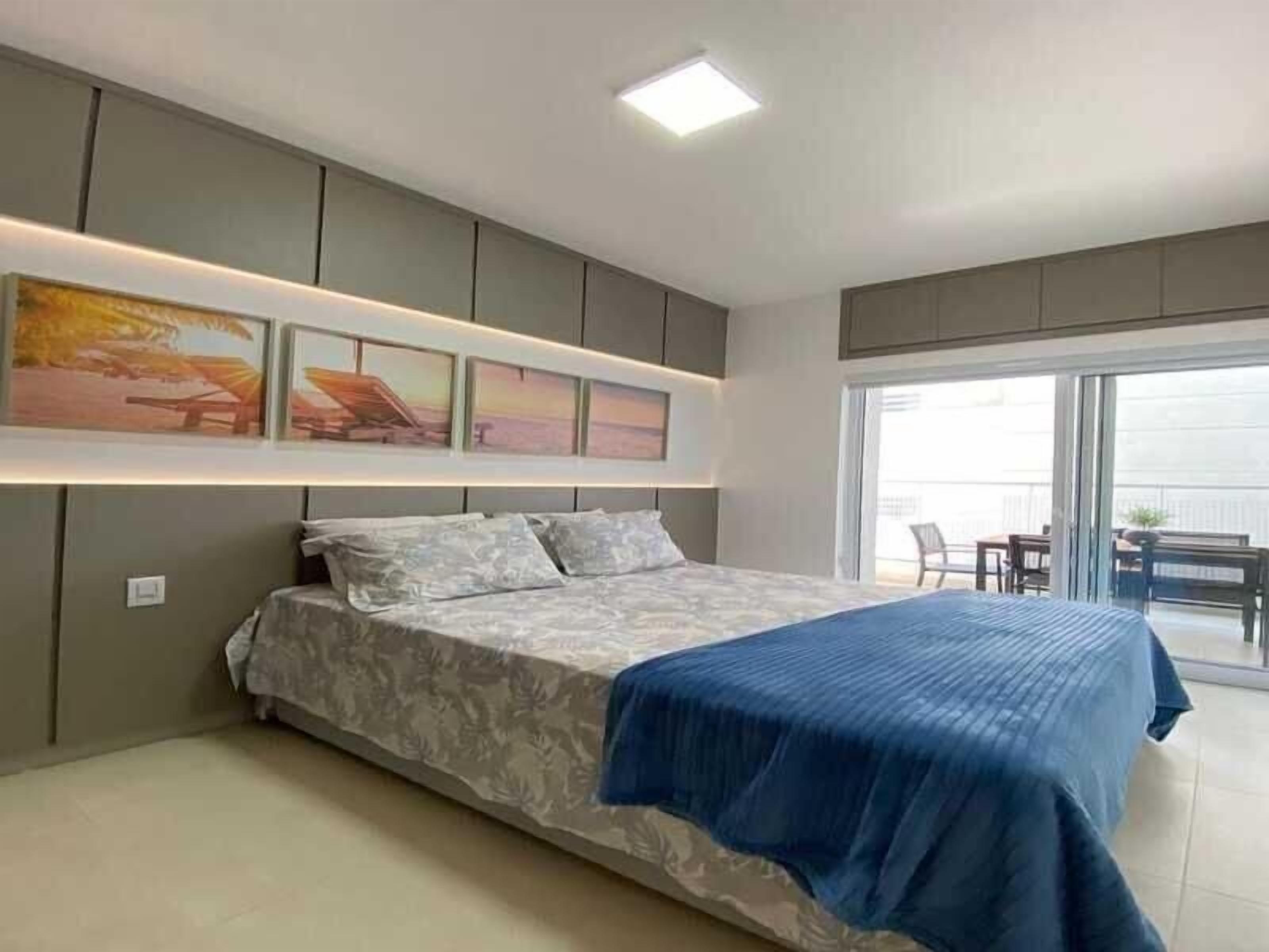 A modern bedroom with a large bed, a ceiling light, and a view of the outside balcony.