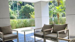 Un espace extérieur moderne, aménagé avec une table ronde et quatre chaises, entouré de grandes fenêtres offrant une vue sur une végétation luxuriante.