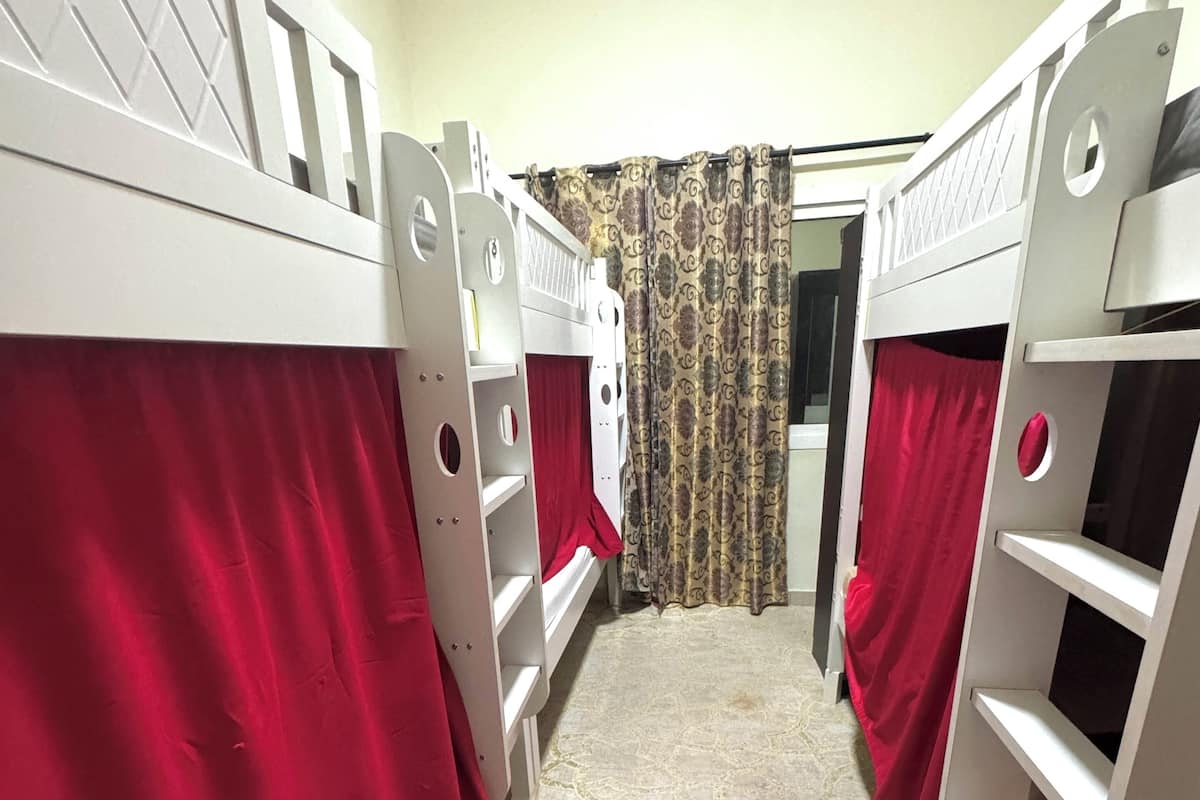 A dormitory room with bunk beds, patterned curtains, and a stone-patterned floor.