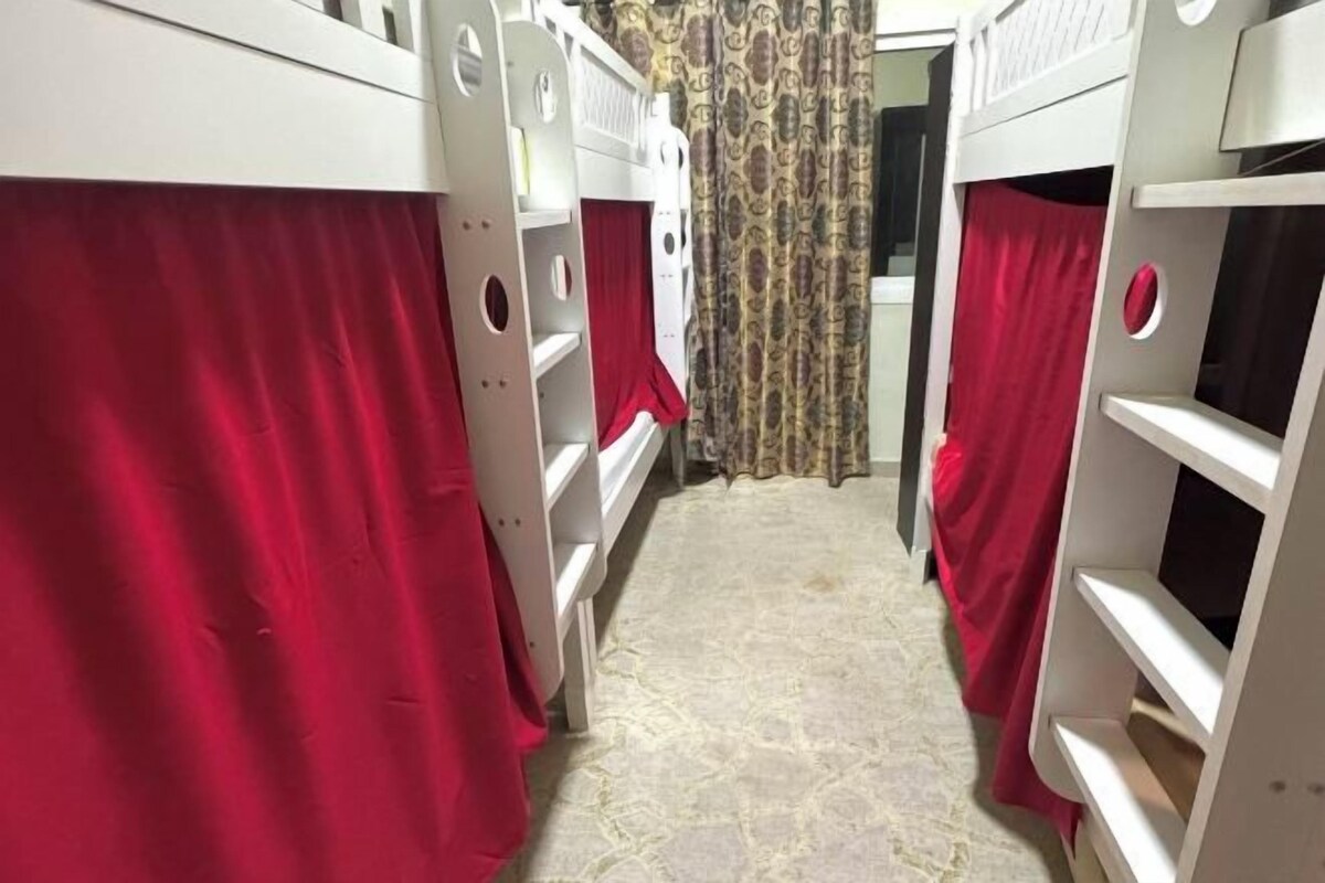 A narrow hallway with bunk beds, each with a red curtain.