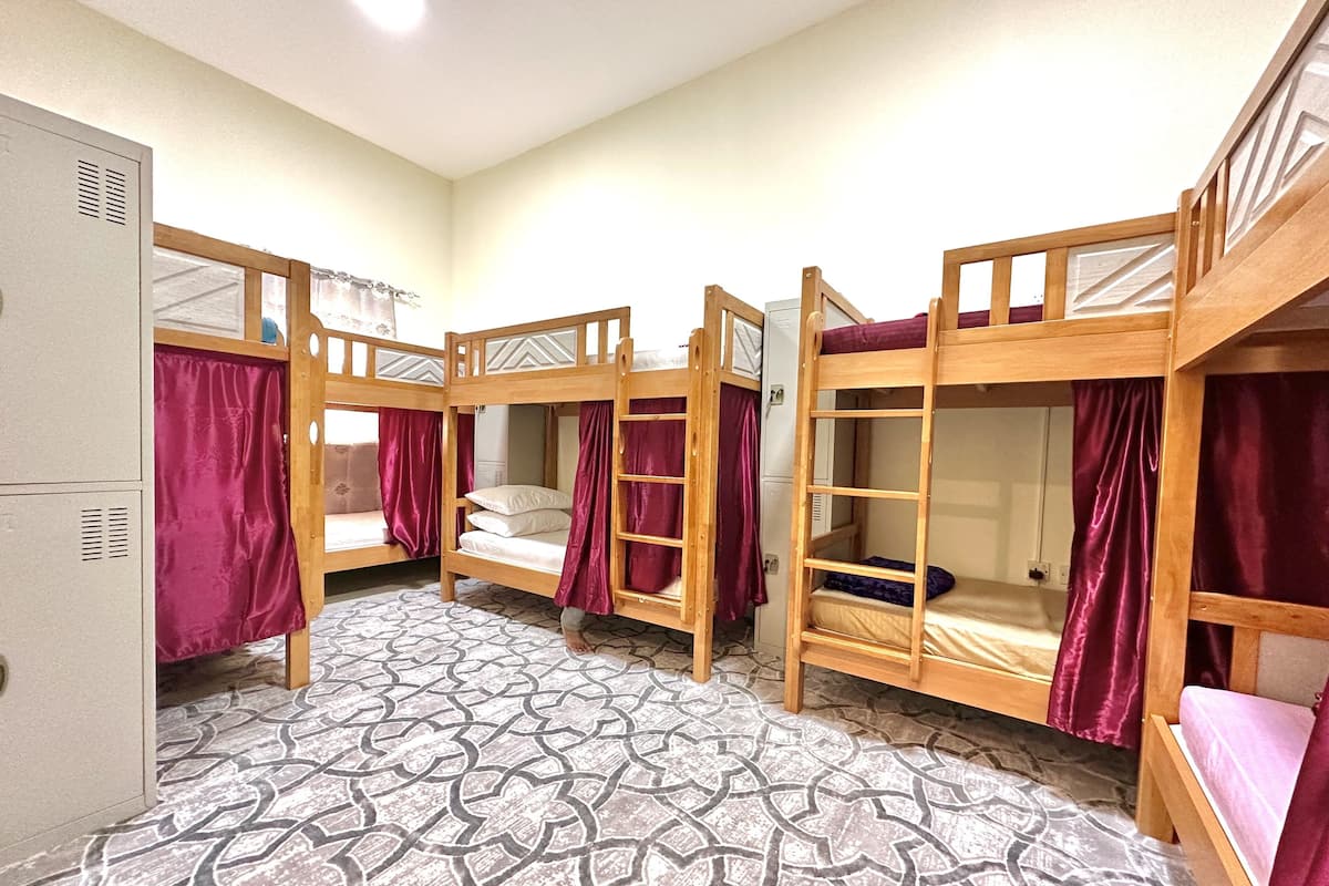 A dormitory room with four bunk beds, a patterned floor, and a white wardrobe.