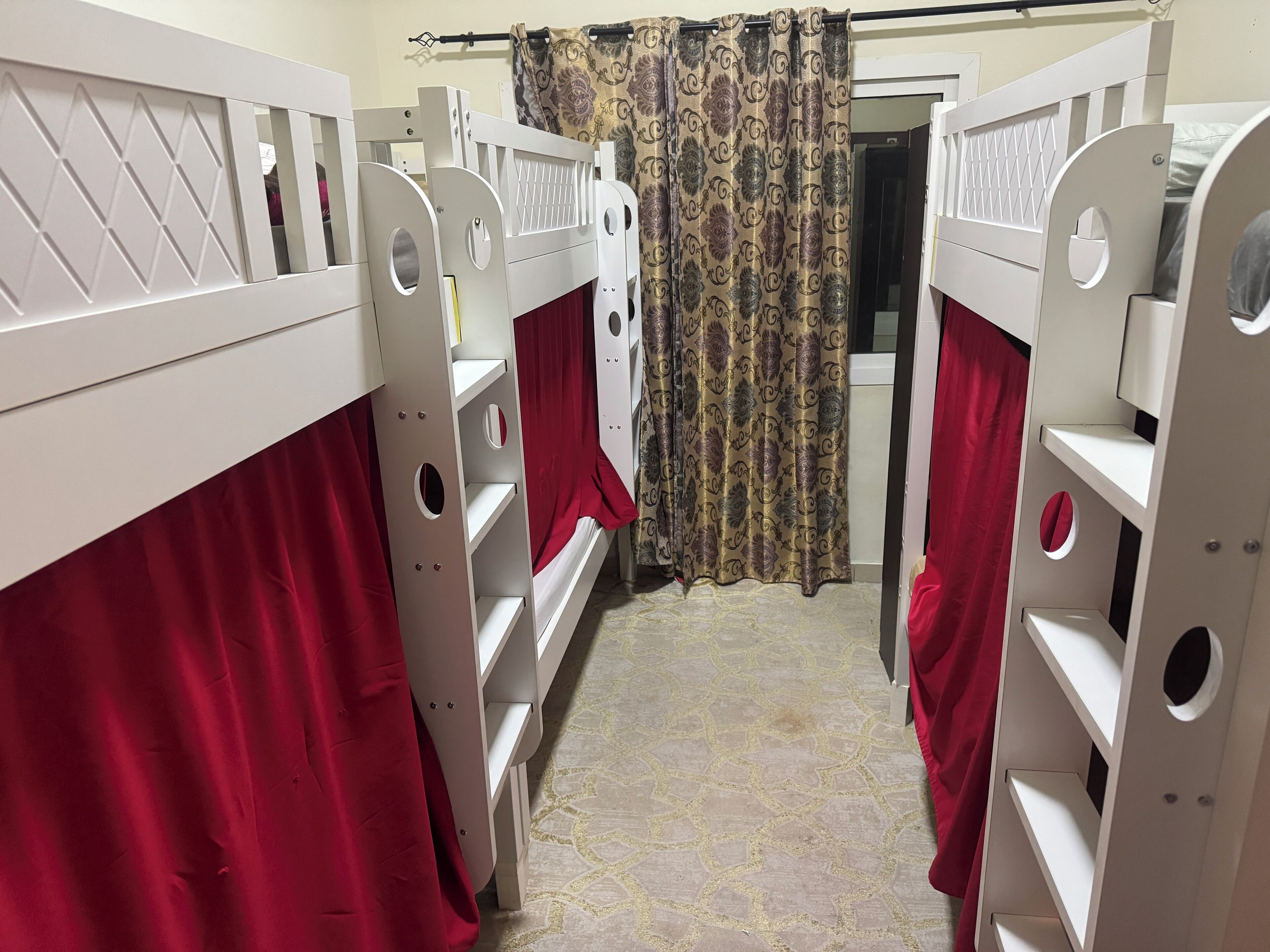 A room with bunk beds, red curtains, and patterned curtains.