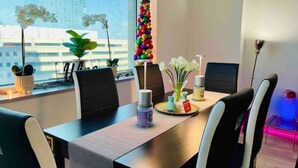 Un espace de bureau moderne avec une longue table, des chaises noires et blanches, une plante en pot, une colonne décorative et une vue sur la ville grâce à de grandes fenêtres.