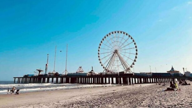 Une plage avec une grande grande roue et une jetée qui s’avance dans l’océan.