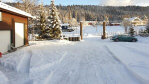 Uma área residencial coberta de neve, com uma casa, um carro e uma grande árvore.