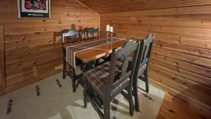 Uma sala de jantar com mesa e cadeiras de madeira, um quadro na parede e um castiçal sobre a mesa.