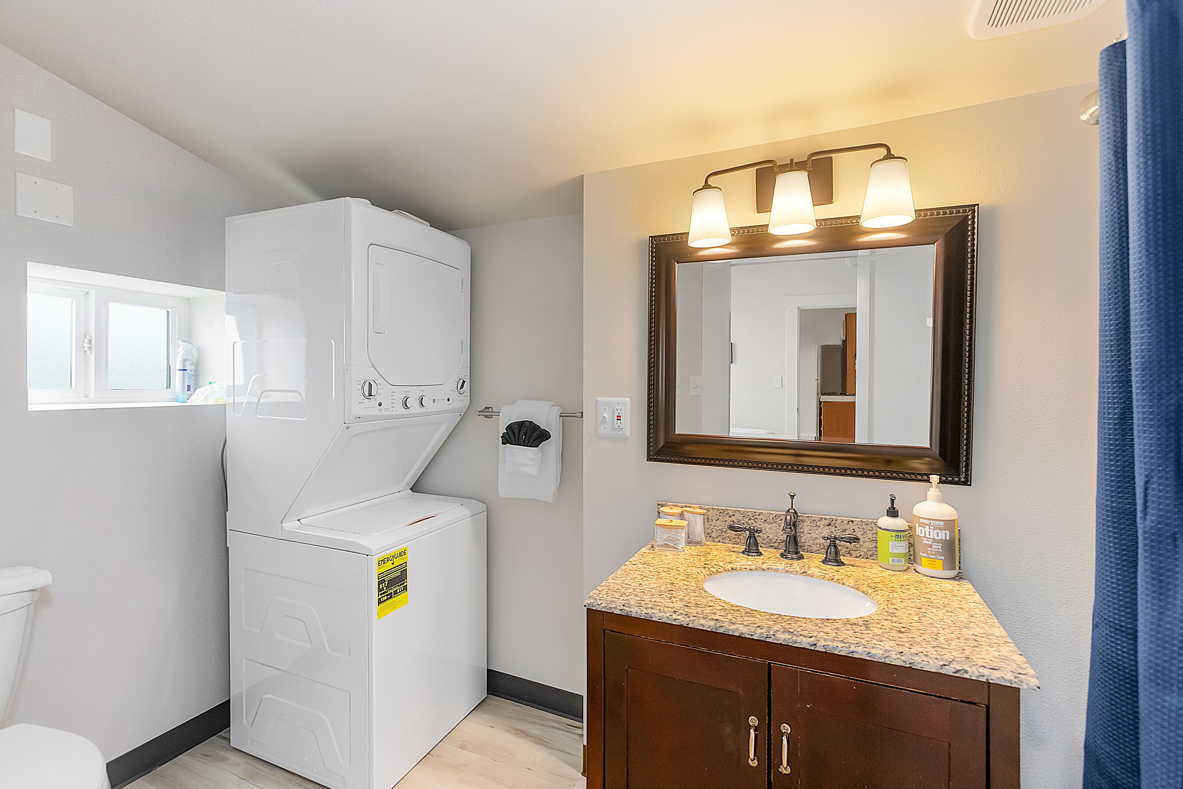 A bathroom with a white washing machine, a sink with a mirror above it, and a window with a view of the outside.
