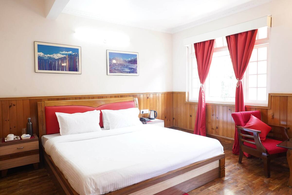 A neatly arranged hotel room with a large bed, wooden paneling, a red chair, and two framed pictures on the wall.