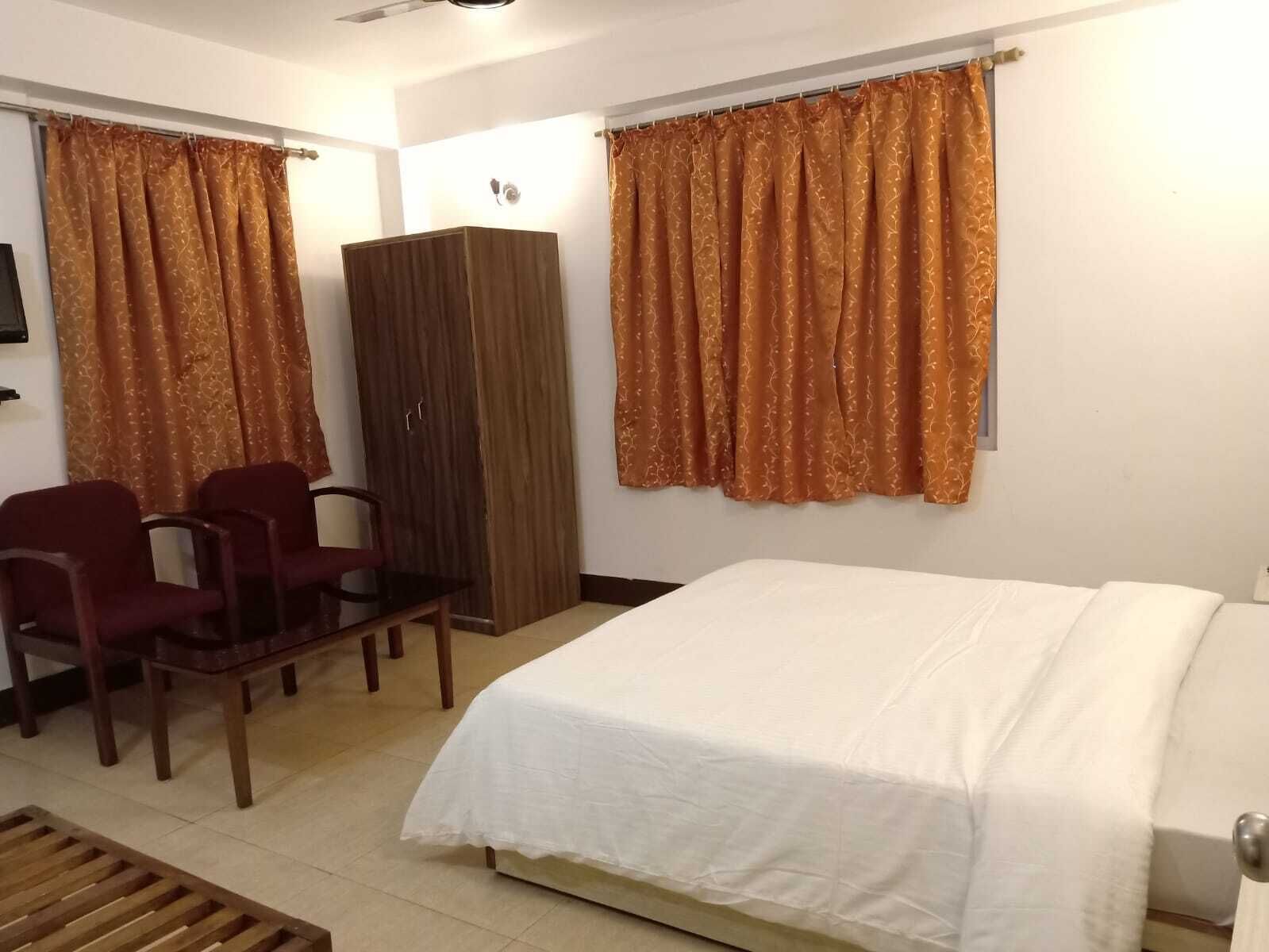 Een hotelkamer met een bed, een houten garderobe, twee rode stoelen en een kleine tafel.