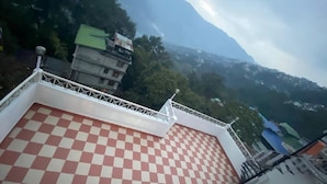 A rooftop with a checkered floor pattern, a white railing, and a view of a mountainous landscape. - Hotel Aster (Gangtok)